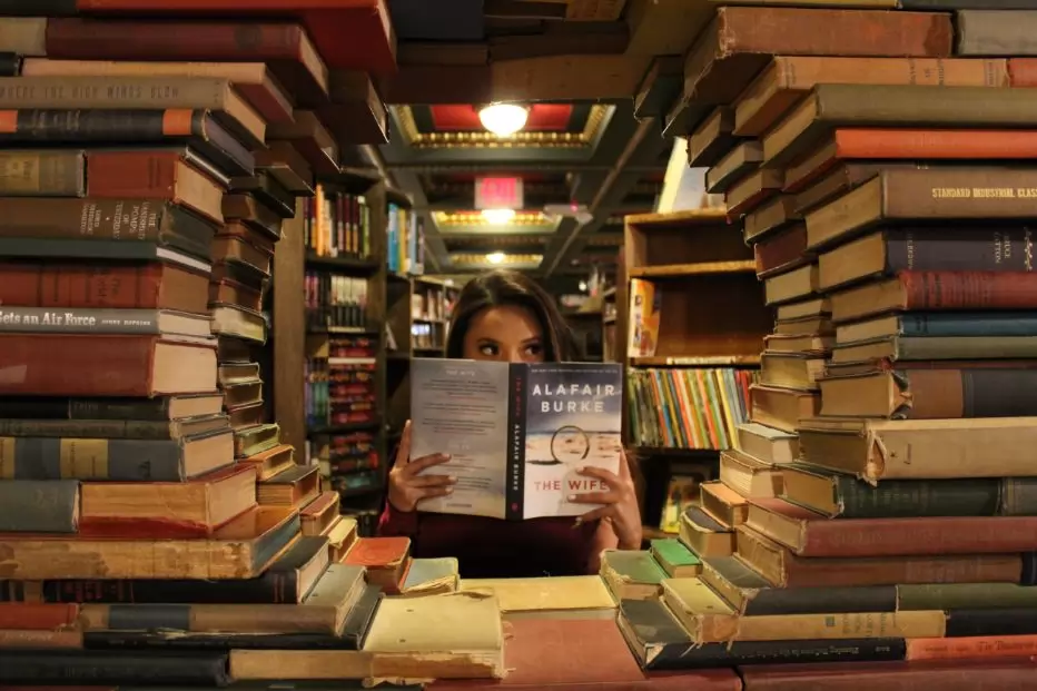 Girl hidden behind a pile of books in a library