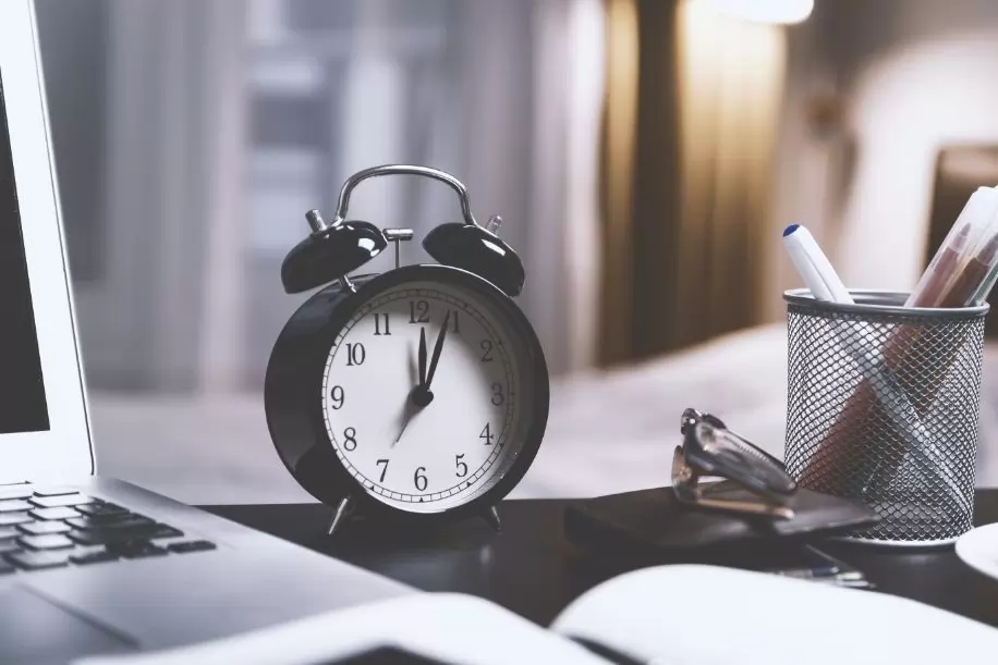 An alarm clock in between stationery on a desk